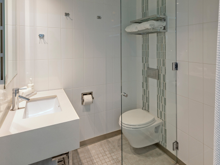 A modern white bathroom with a wall-mounted sink, a glass shower enclosure, a wall toilet, and minimalist tile walls and floor.