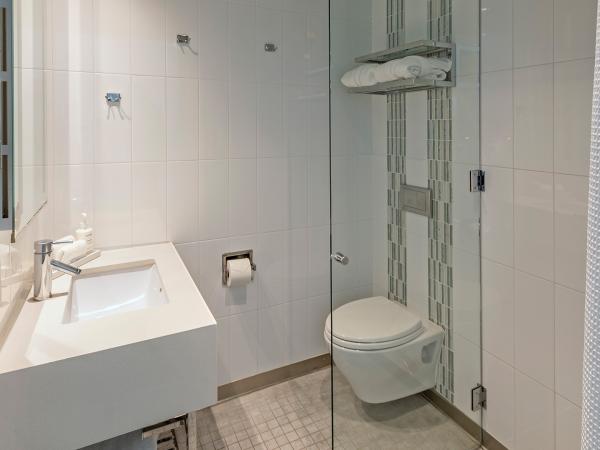 A modern white bathroom with a wall-mounted sink, a glass shower enclosure, a wall toilet, and minimalist tile walls and floor.