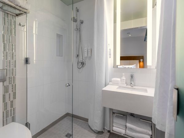 A modern white bathroom with a glass shower, tiled walls, a sink with storage below, a large mirror, and a white curtain on the right side.