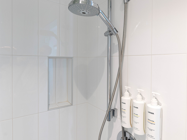 A modern shower with a rainhead, handheld wand, tiled walls, and three shampoo/conditioner bottles in a built-in niche.
