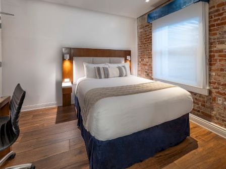 A cozy hotel room with a king bed, exposed brick wall, desk and chair, wall-mounted TV, nightstands, and soft lighting. End.