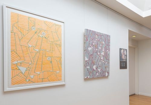 Abstract geometric paintings on a white gallery wall, featuring orange, purple, and dark patterned shapes in frames. End.