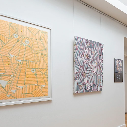 Abstract geometric paintings on a white gallery wall, featuring orange, purple, and dark patterned shapes in frames. End.