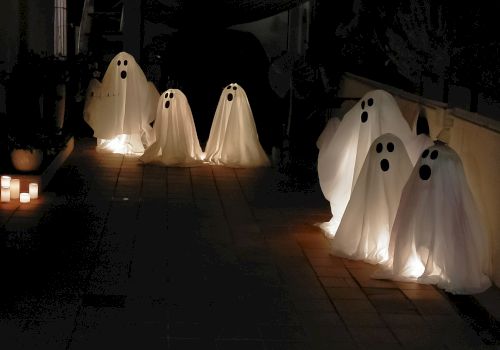 Silhouetted ghostly figures drift along a dark path, illuminated by warm lanterns, creating a spooky, seaside funeral-like procession.