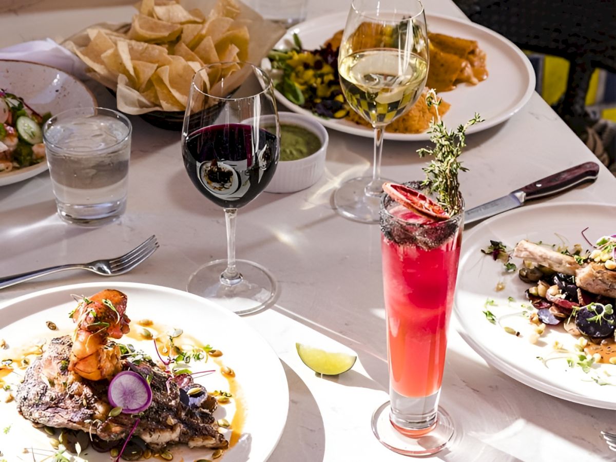 A festive dinner table with plates of food, bread, and wine and pink cocktails in glasses.