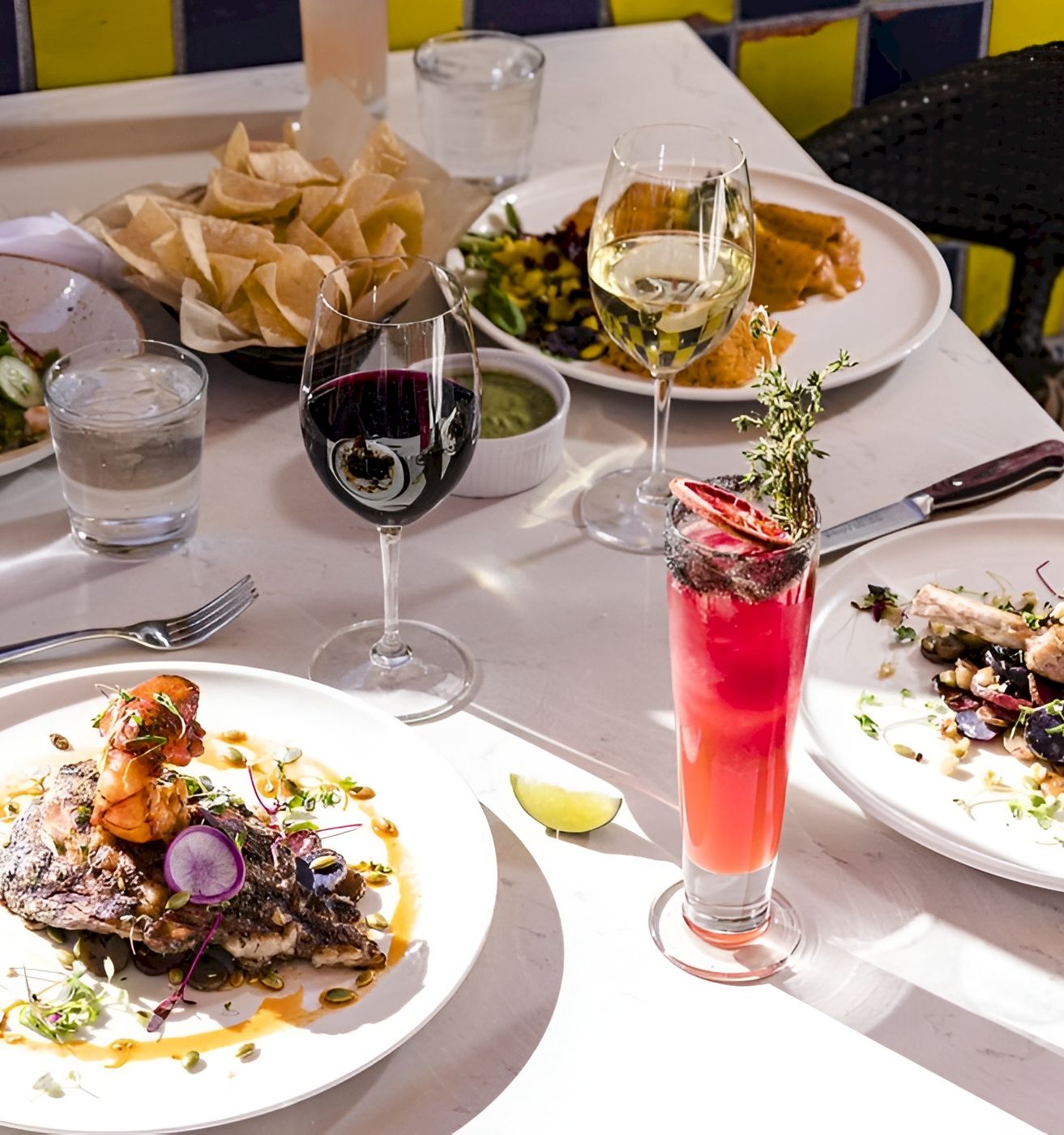 A festive dinner table with plates of food, bread, and wine and pink cocktails in glasses.