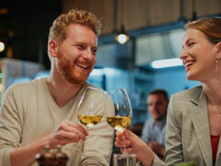 Two friends toast wine glasses, smiling and enjoying a cozy night out together.