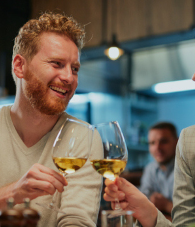 Two friends toast wine glasses, smiling and enjoying a cozy night out together.