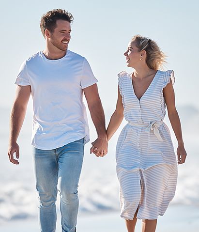 A couple walking hand in hand on the beach, smiling and enjoying a sunny day by the ocean.