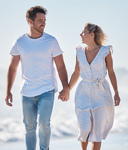 A couple walking hand in hand on the beach, smiling and enjoying a sunny day by the ocean.