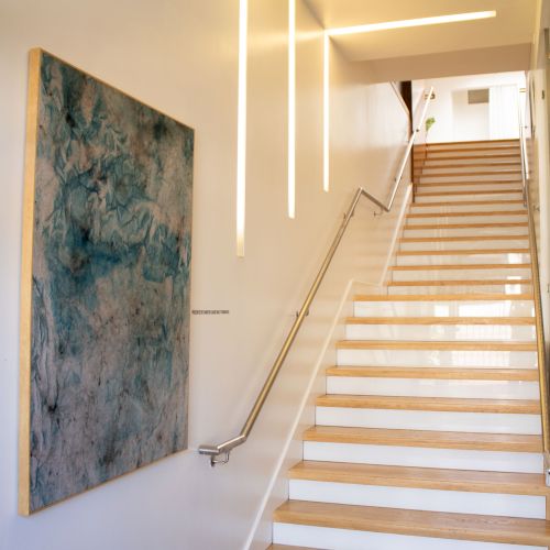 A bright stairwell with light strips on the wall, a blue abstract painting, and clean, modern railings leading up the stairs.