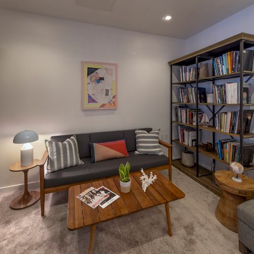 Cozy living room with two tall bookshelves, a gray sofa, a wooden coffee table, side tables, a small lamp, framed art, and a plush rug.