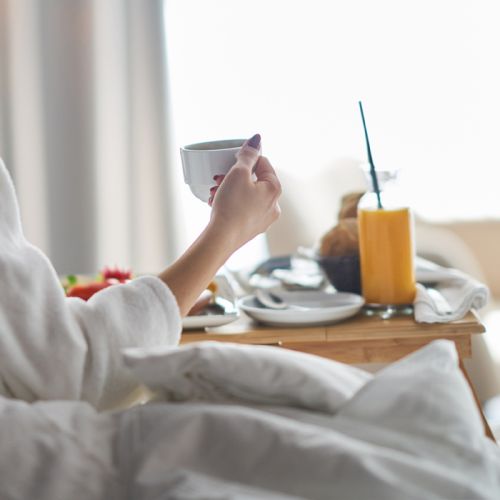 Someone in bed with a breakfast tray: cup, orange juice, fruit, toast, and a small bowl, ready to eat.