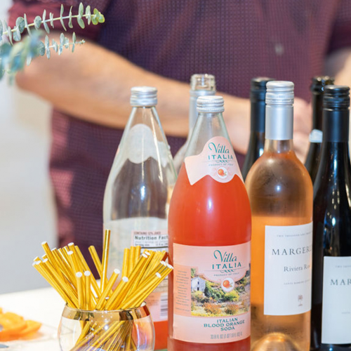 A vibrant table of beverages and condiments: hot sauces, soda, beer, and a glossy bottle assortment, with a colorful background and festive vibe.