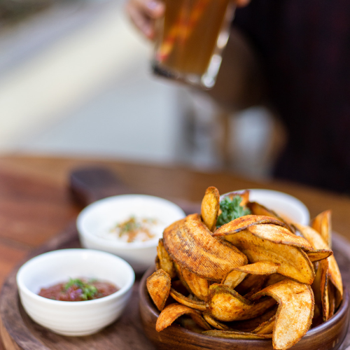 Terminal bar scene with a glass of beer and a wooden plate of crispy potato wedges with a dipping sauce and herbs, on a rustic table.