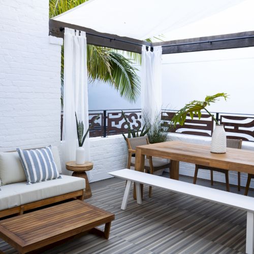 A cozy balcony with a wooden bench, cushions, and a small table; looks like a sunny, relaxing outdoor seating area.