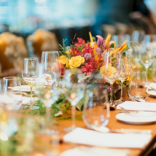 A long dining table set for a formal event with elegant floral centerpieces, glassware, plates, and cutlery ready for guests to arrive.