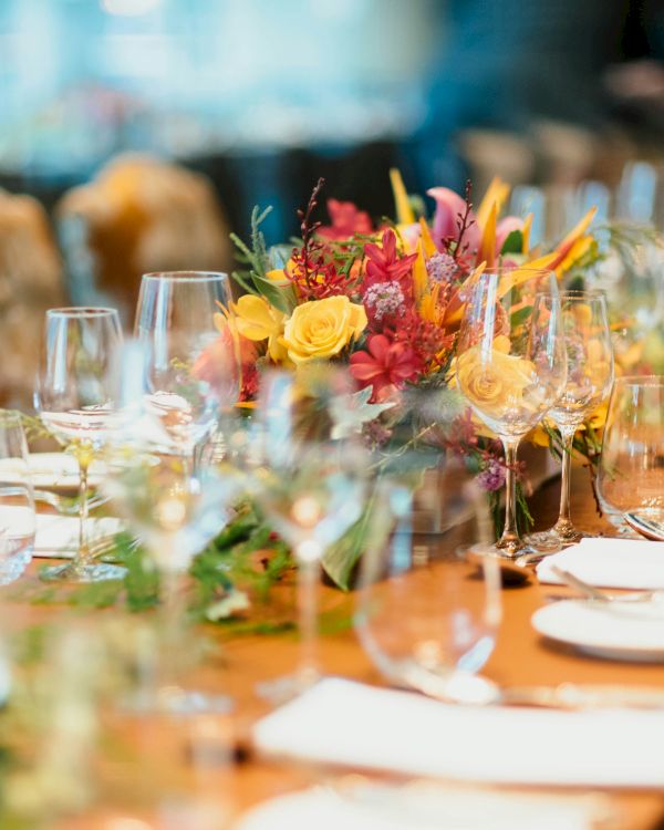 A long dining table set for a formal event with elegant floral centerpieces, glassware, plates, and cutlery ready for guests to arrive.