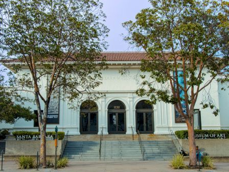 The Santa Barbara Museum of Art building with arches and stairs, framed by trees under a clear blue sky.