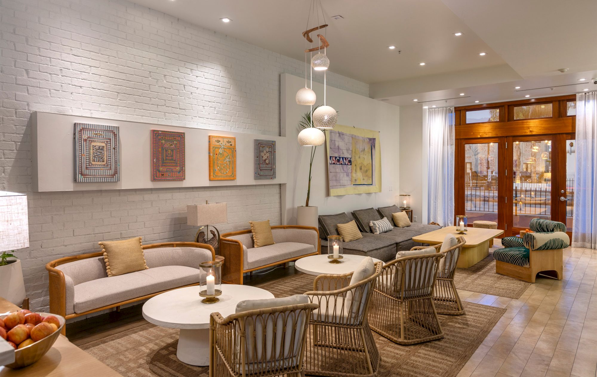 Bright modern lounge with rattan chairs, sofas, framed wall art, pendant globe lamps, and glass doors opening to a patio.
