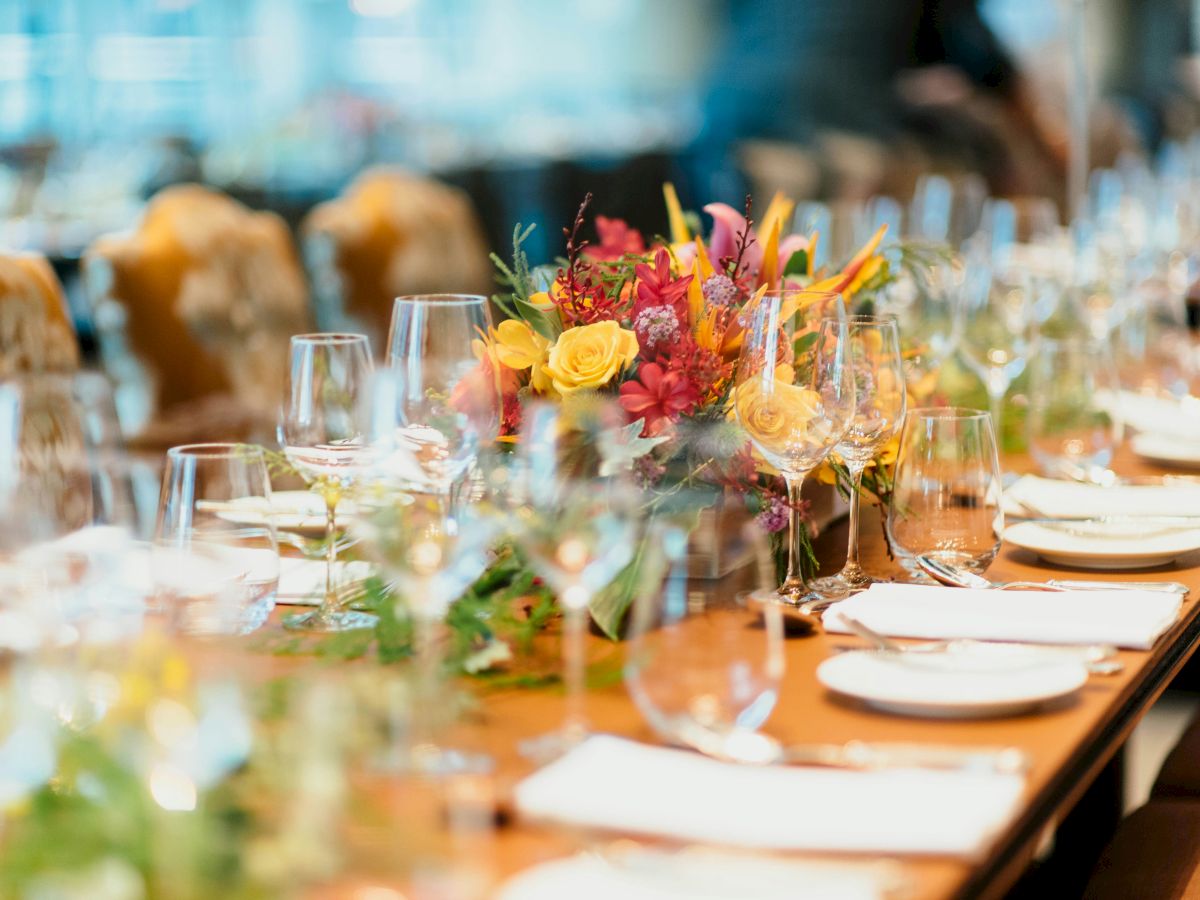A banquet table with a colorful flower centerpiece and glassware, set for a celebration outdoors.